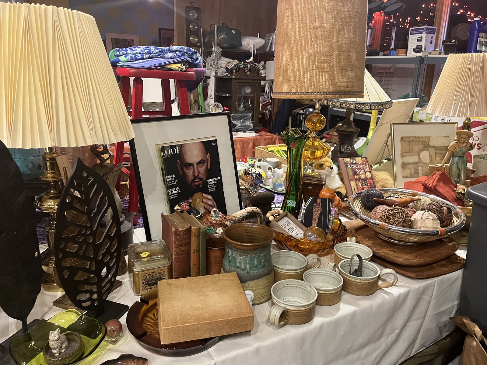 Stoneware mugs and pitcher, a framed vintage LOOK magazine cover, amber glass and a burlap shade lamp on a sale table